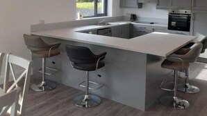 A modern kitchen with grey cabinets, a central island with bar stools, and a wall-mounted clock. - Stable Hill House,
5km from Killarney Town
Private & Peaceful Location
 (Killarney)