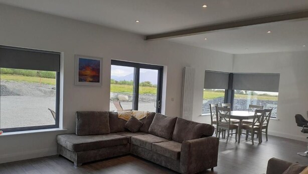 A modern living room with a sectional sofa, a dining table with chairs, large windows with a view of the outdoors, and a painting on the wall. - Stable Hill House,
5km from Killarney Town
Private & Peaceful Location
 (Killarney)