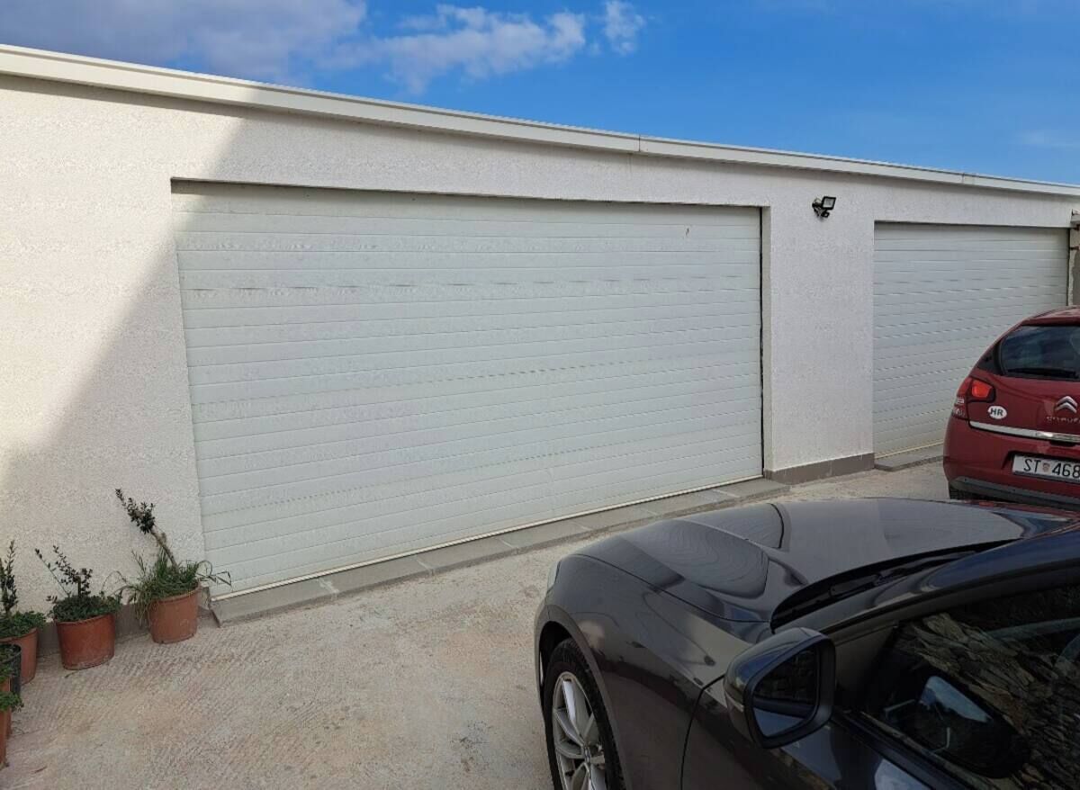 En bygning med to lukke garageporte, en rød bil parkeret, og flere krukker med planter nær indgangen.