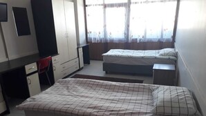 Un dormitorio con cama, escritorio, silla, armario y ventana con cortinas.