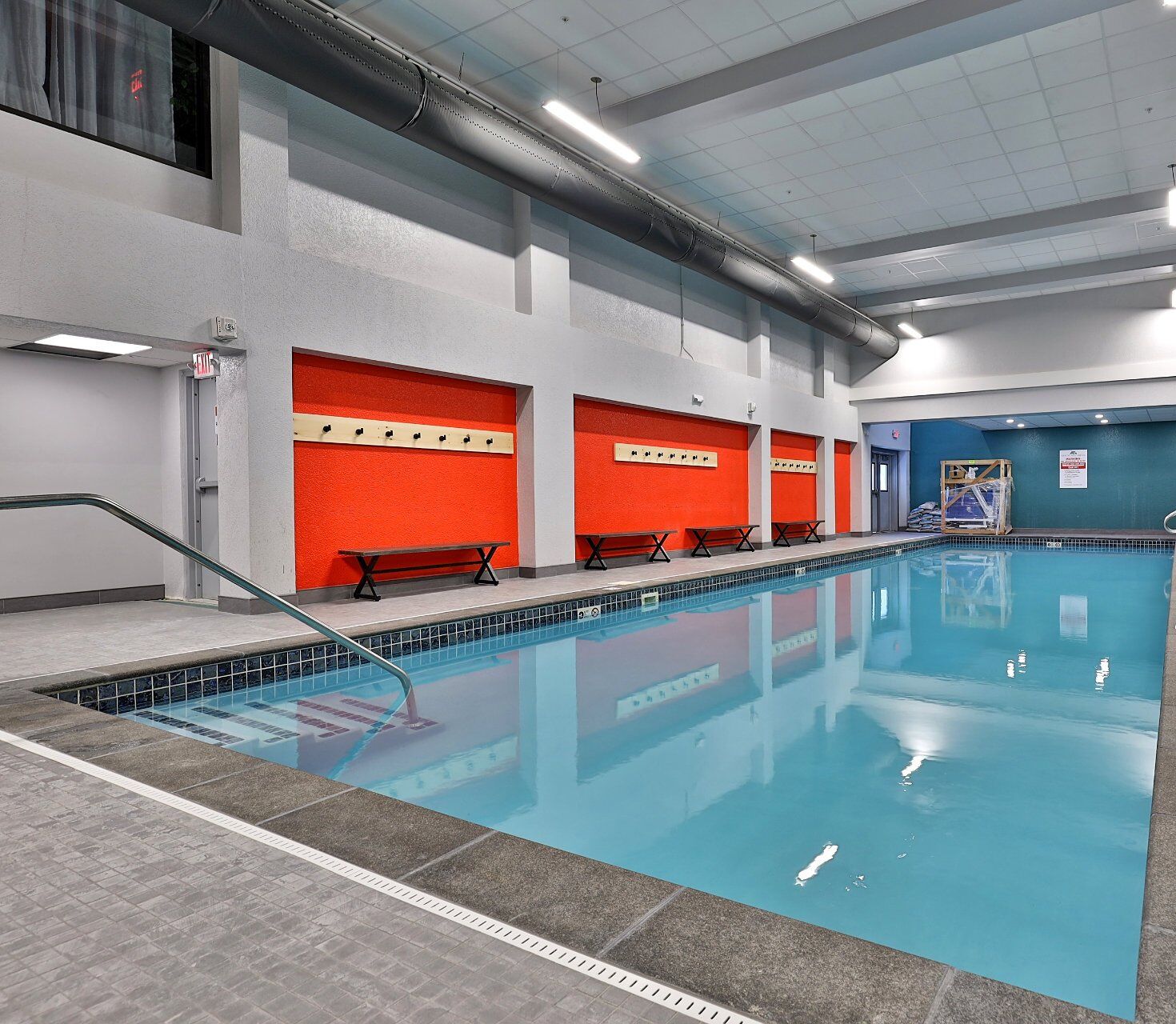 Une piscine intérieure à l’eau claire, avec des bancs le long du mur et un sol carrelé.