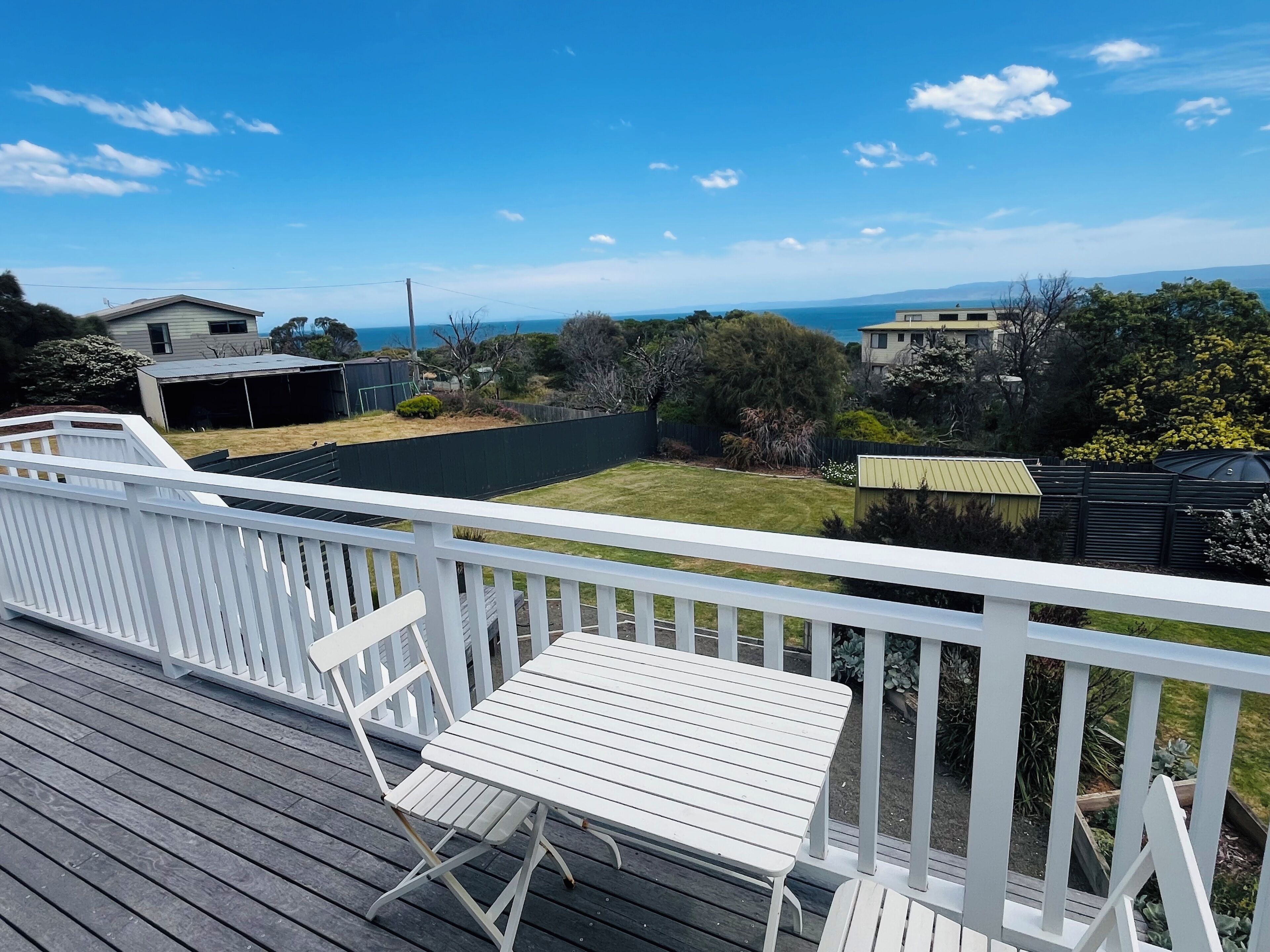 A deck with white railings, a white table, and a white chair.