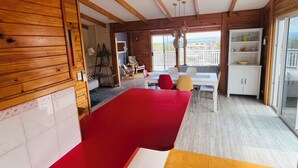 Una habitación con un sofá rojo, una mesa blanca y una alfombra amarilla. Hay un balcón con barandilla y vistas al exterior.