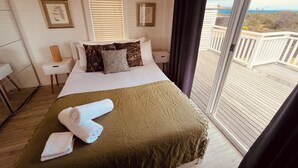Un dormitorio con cama, mesita de noche, lámpara y vistas al exterior.
