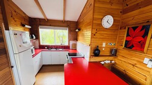 Una cocina compacta con paredes de madera, encimera roja, refrigerador blanco y una ventana con vistas a zonas verdes.