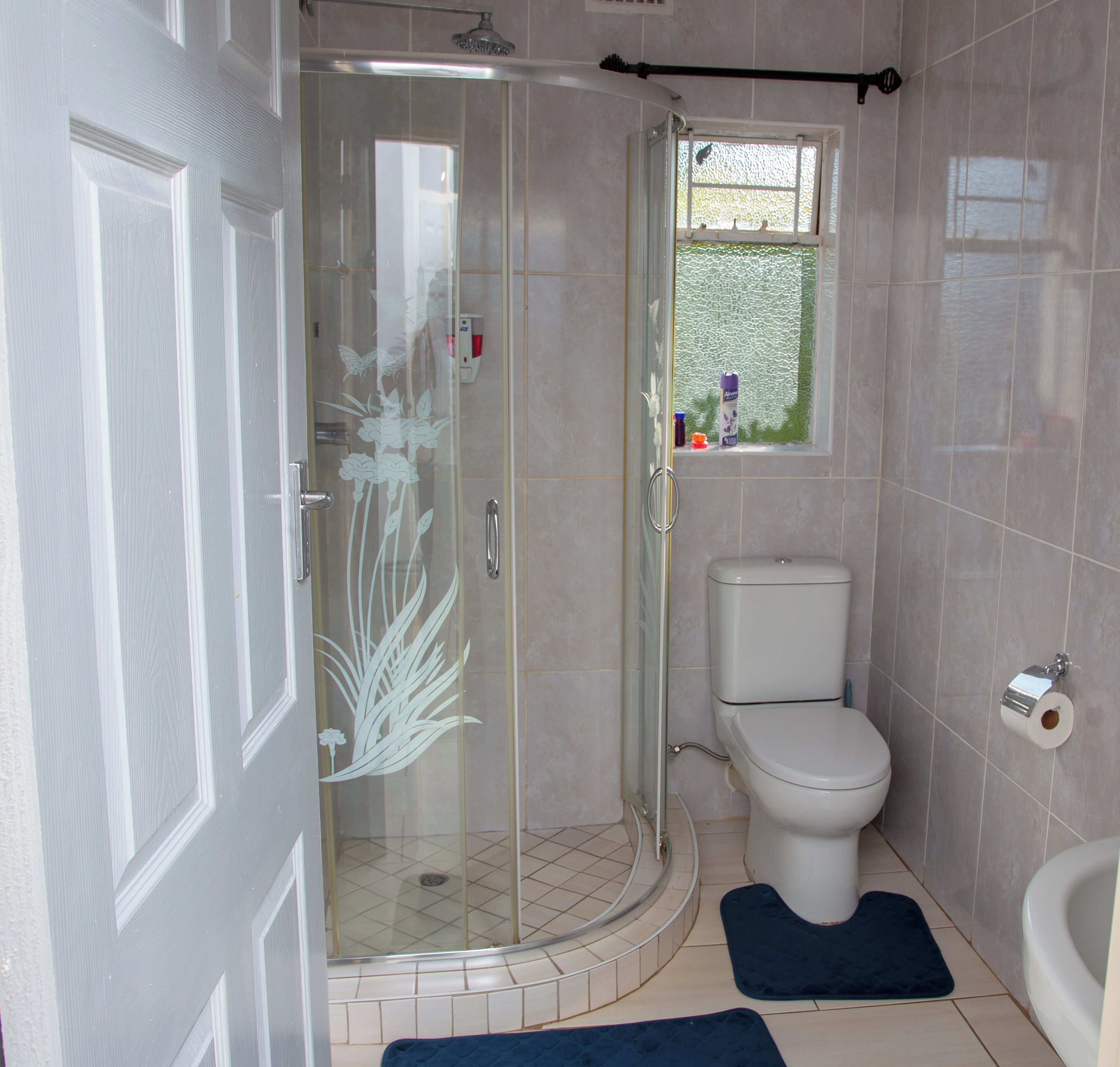 A modern bathroom with a glass shower enclosure, a toilet, and a small window.
