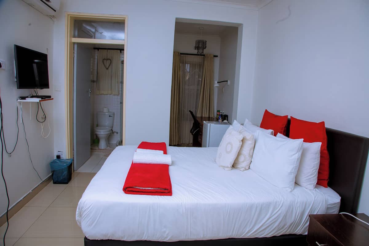 A hotel room with a bed, a TV, a bathroom, and a shower area.