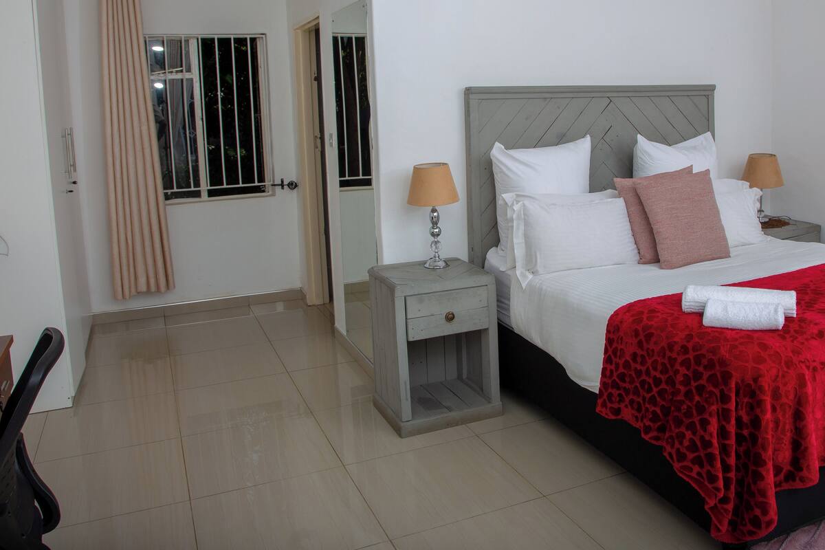 A hotel room with a bed, two bedside tables with lamps, a chair, and a desk.