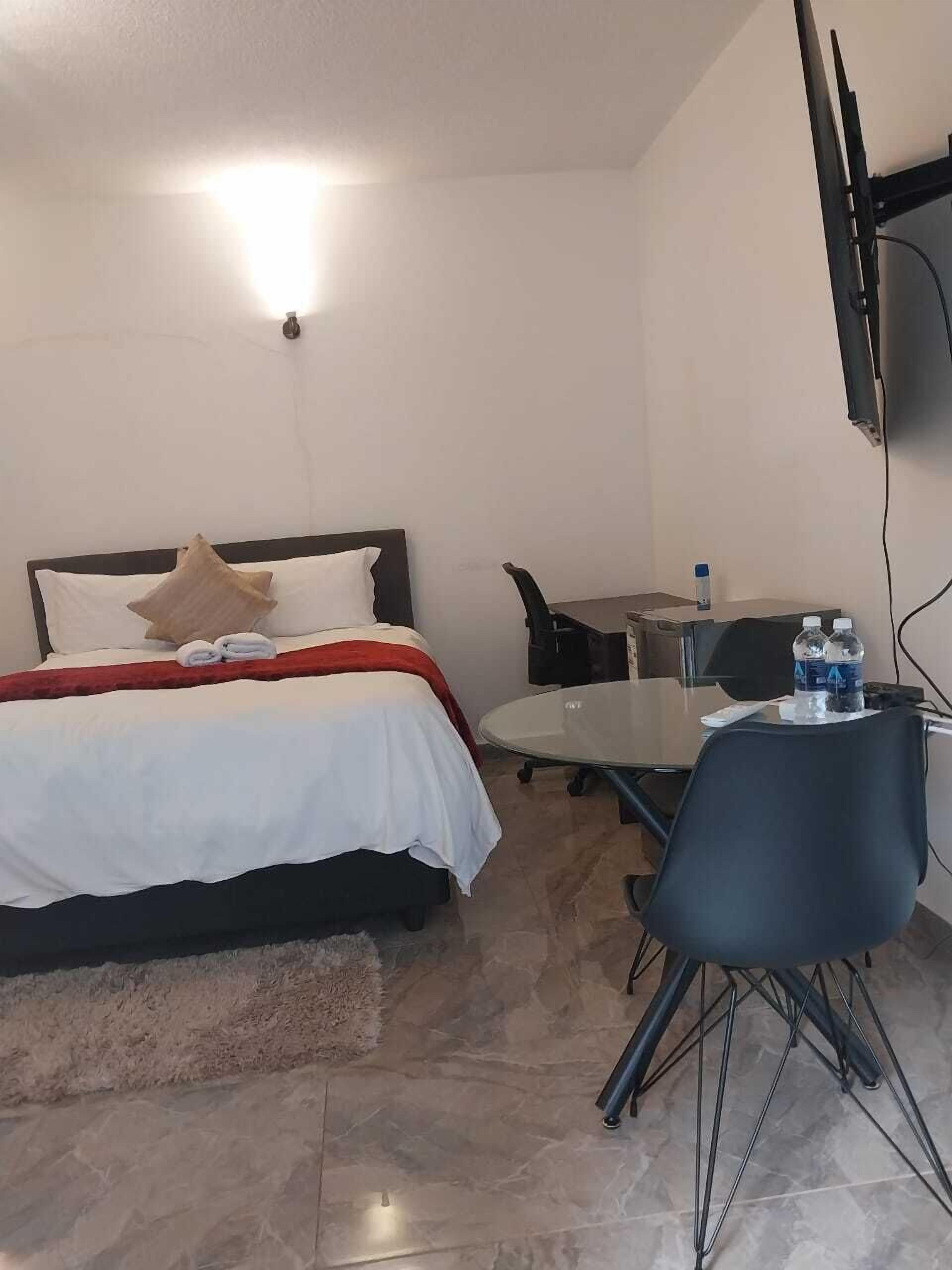 Habitación de hotel con cama, escritorio, silla, televisor y una botella de agua.