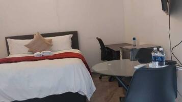 A hotel room with a bed, a desk, a chair, a TV, and a water bottle.