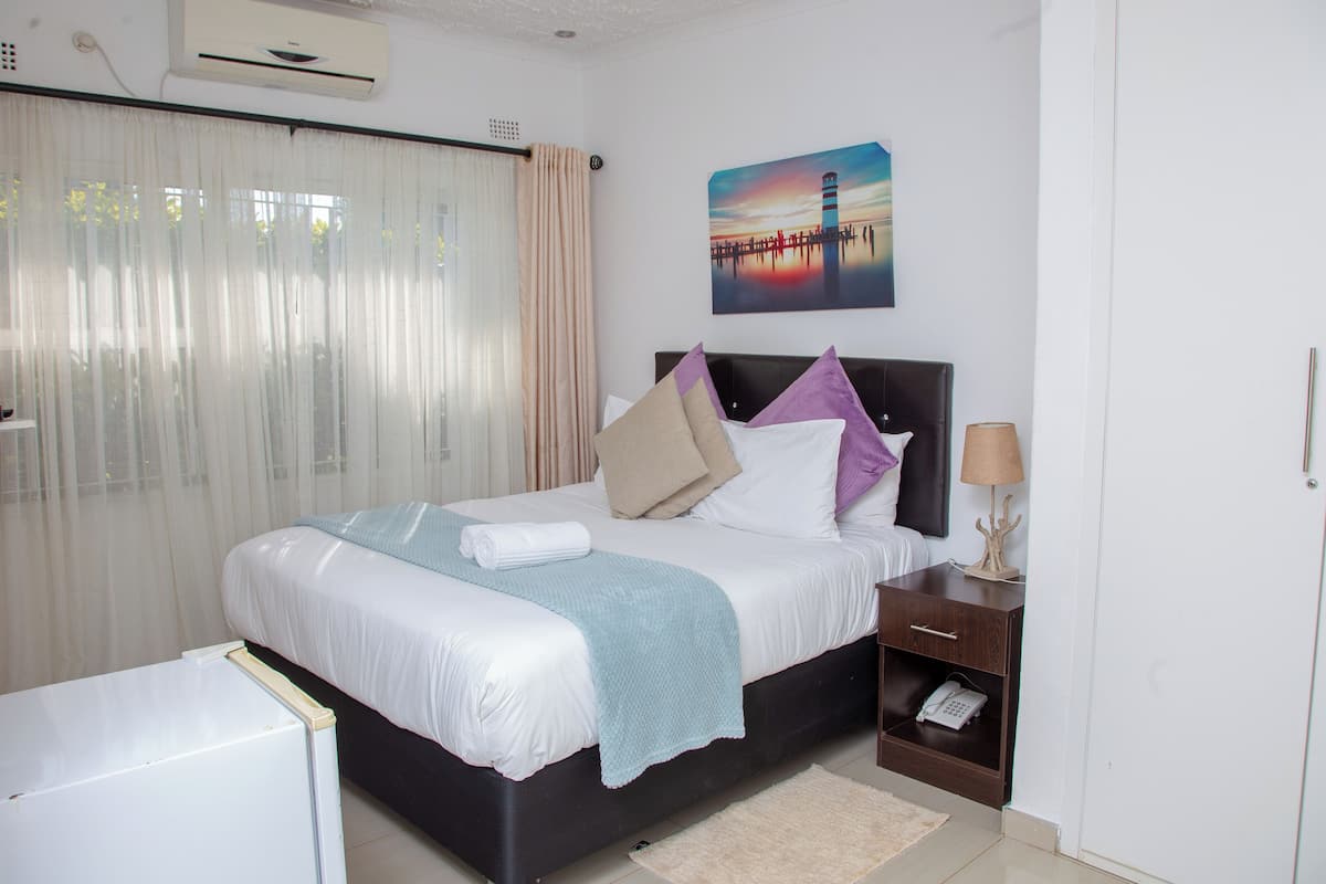 A neatly arranged hotel room with a bed, bedside table, lamp, and a painting on the wall.