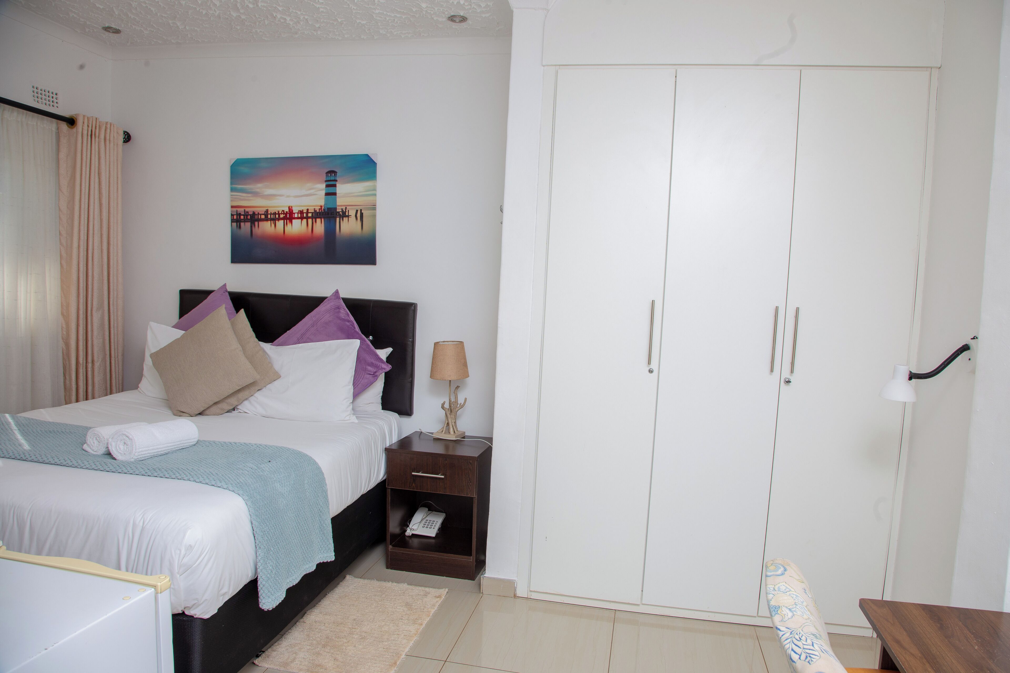 A bedroom with a bed, nightstand, wardrobe, and a painting on the wall.