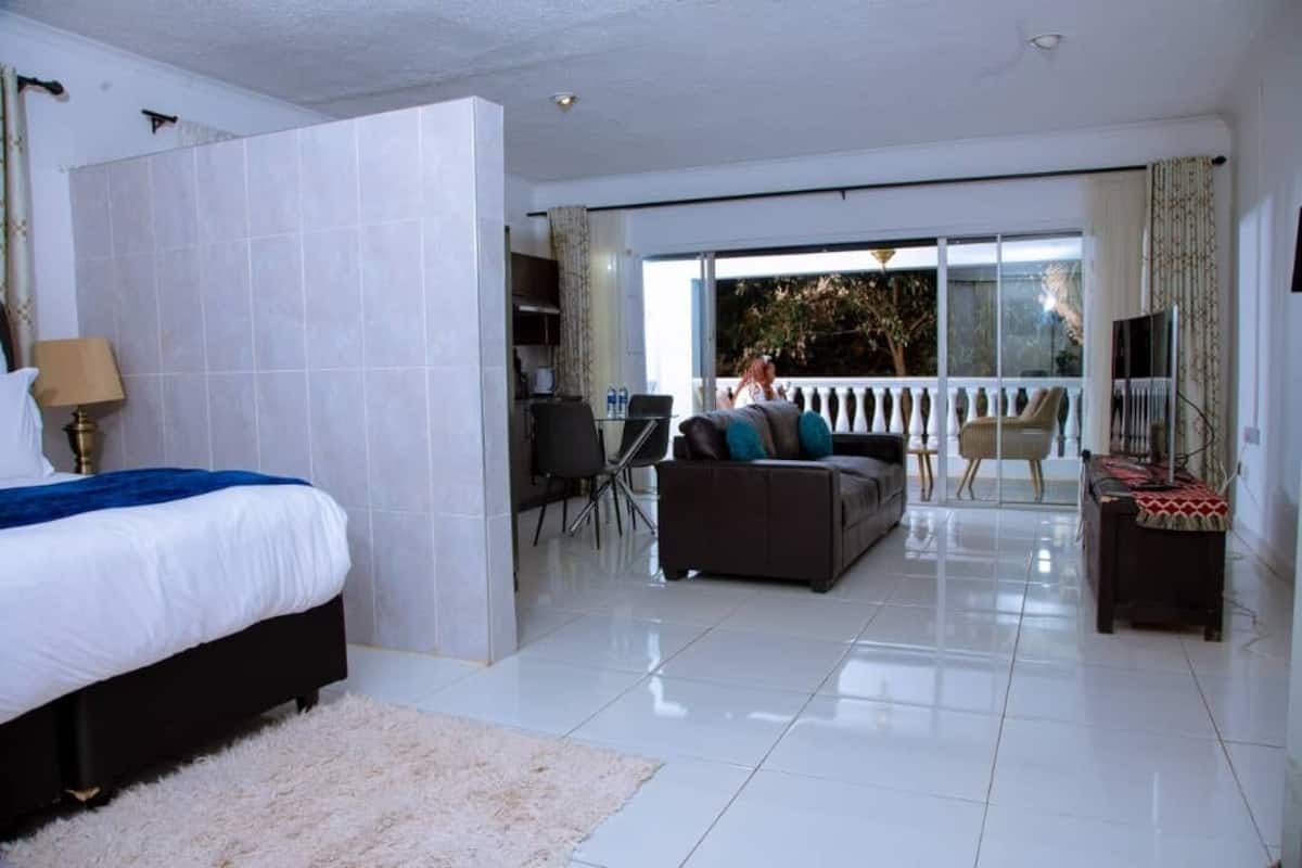 A hotel room with a bed, a sofa, a dining table, and a balcony with a view.