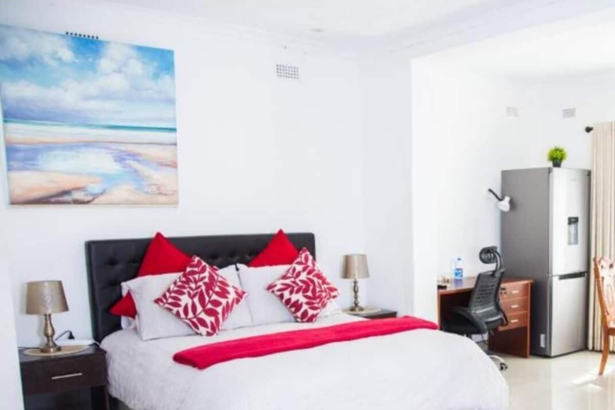 A hotel room with a bed, a desk, a chair, a refrigerator, and a painting on the wall.