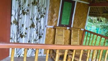 A wooden balcony with a thatched roof, a wooden railing, and a view of a bamboo structure.