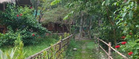 A rustic garden with a bamboo fence, a thatched-roof structure, and lush greenery.