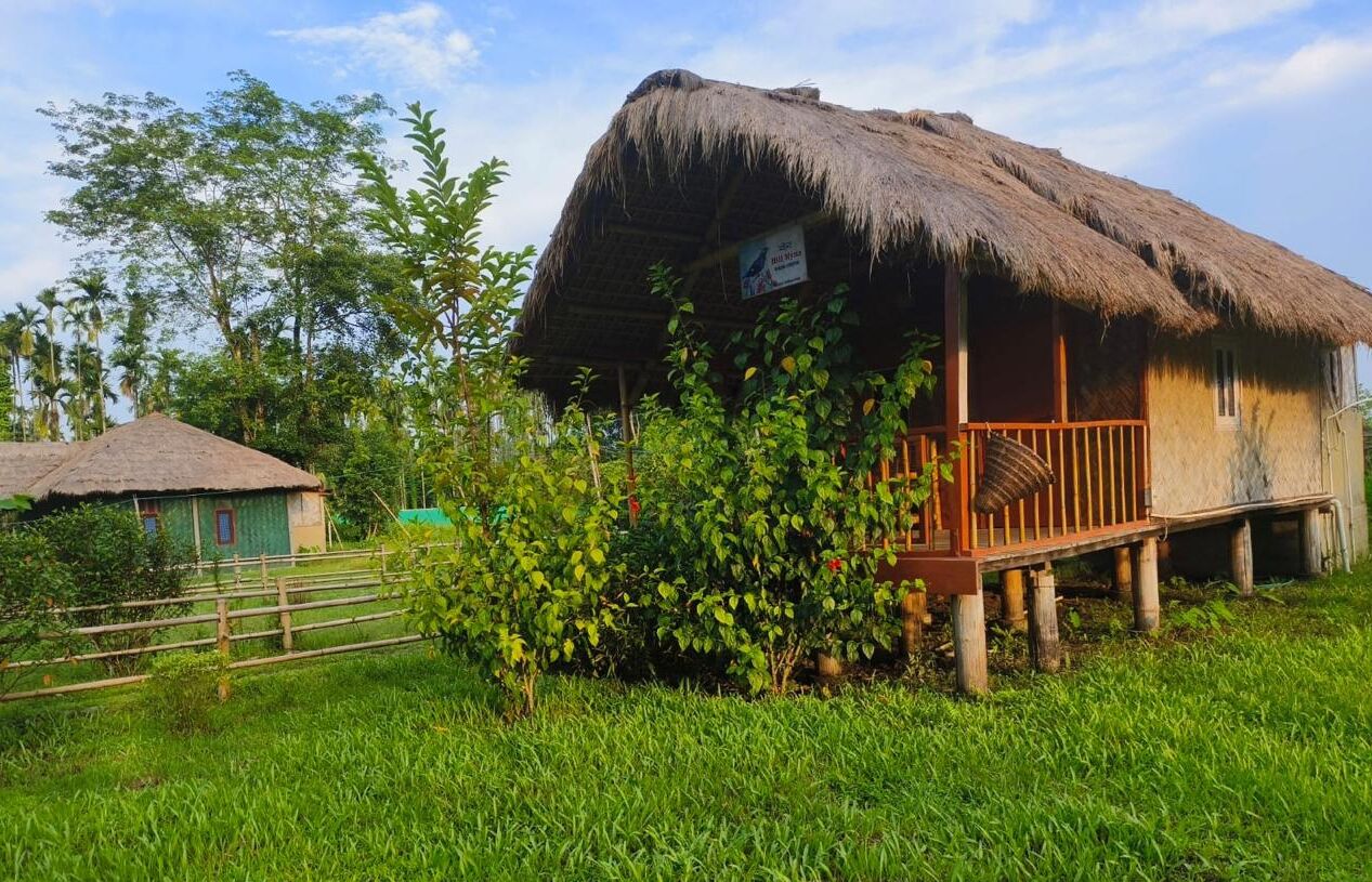 A thatched-roof house with a wooden deck and a signboard.