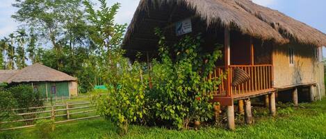 A thatched-roof house with a wooden deck and a signboard.