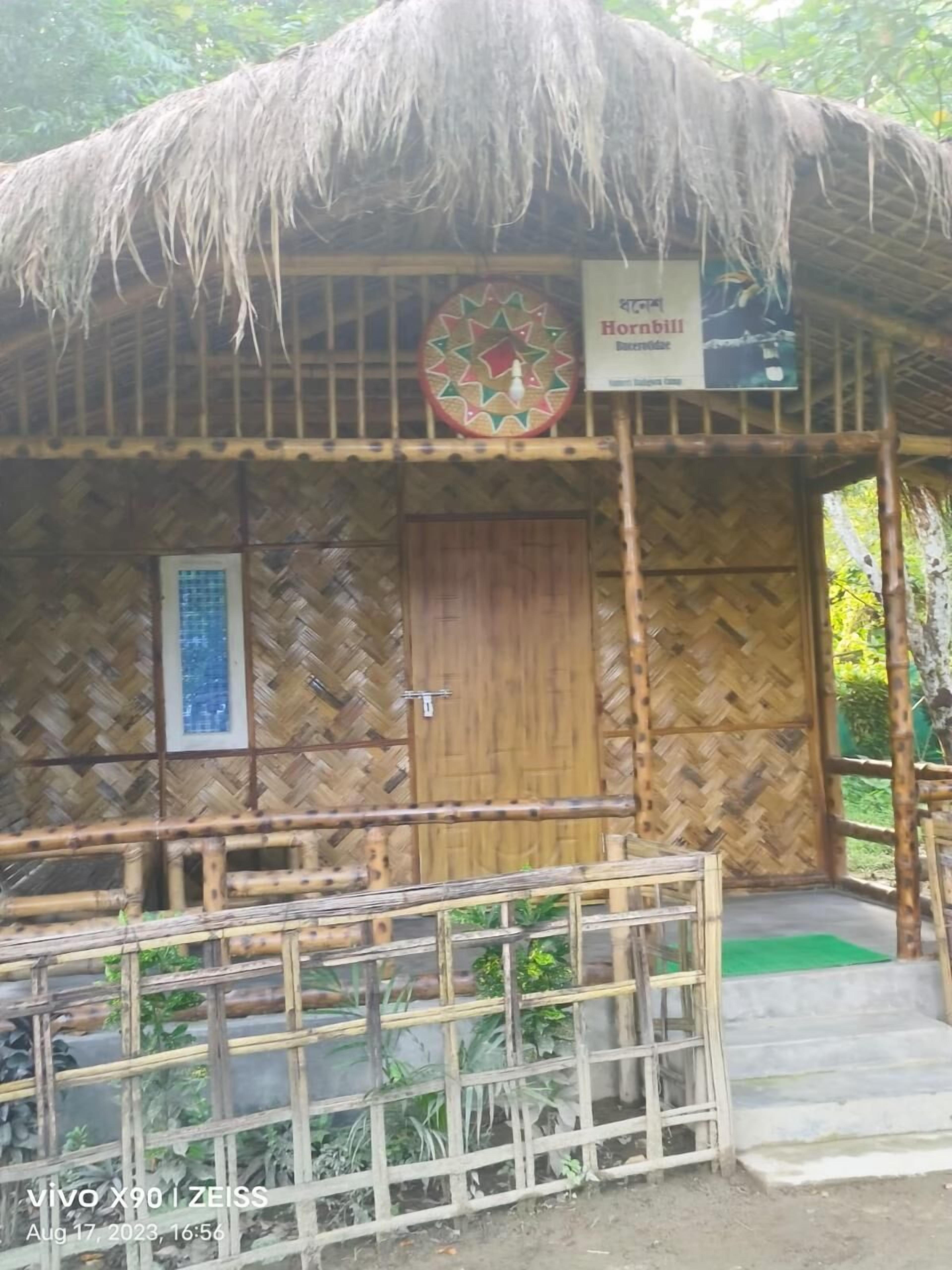 A thatched-roof hut with a wooden door, a signboard, and a bamboo fence in front.