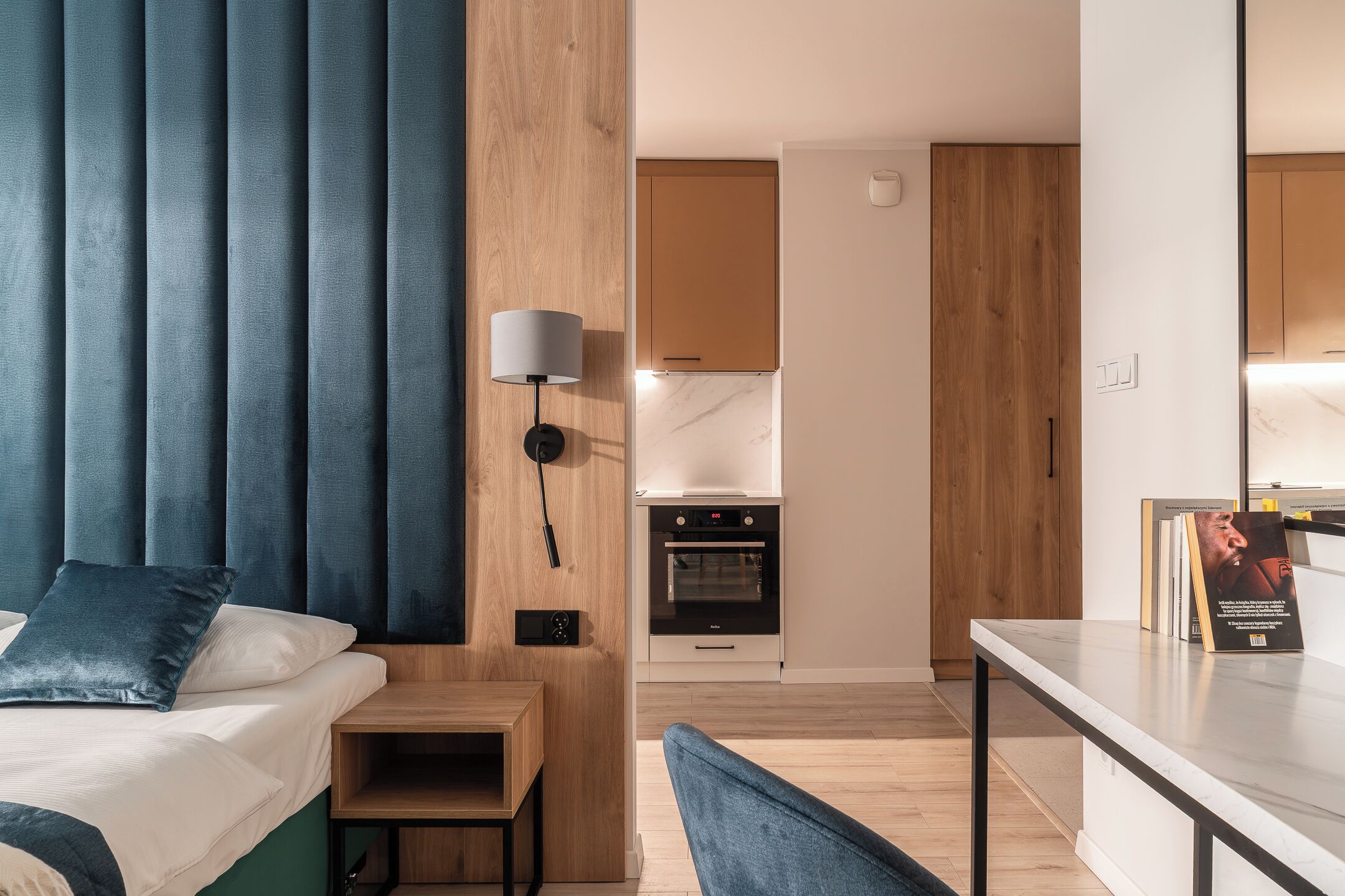 Una habitación de hotel moderna con cama, mesita de noche, lámpara y vistas a la cocina.