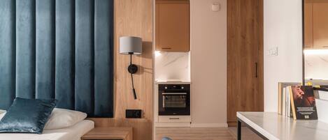Una habitación de hotel moderna con cama, mesita de noche, lámpara y vistas a la cocina.