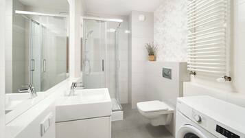 Un baño moderno con ducha envuelta en vidrio, inodoro y lavadora.