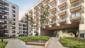 A modern apartment building with multiple balconies, a covered walkway, and landscaped areas with plants. - Symphony Atal City Square (Wroclaw)