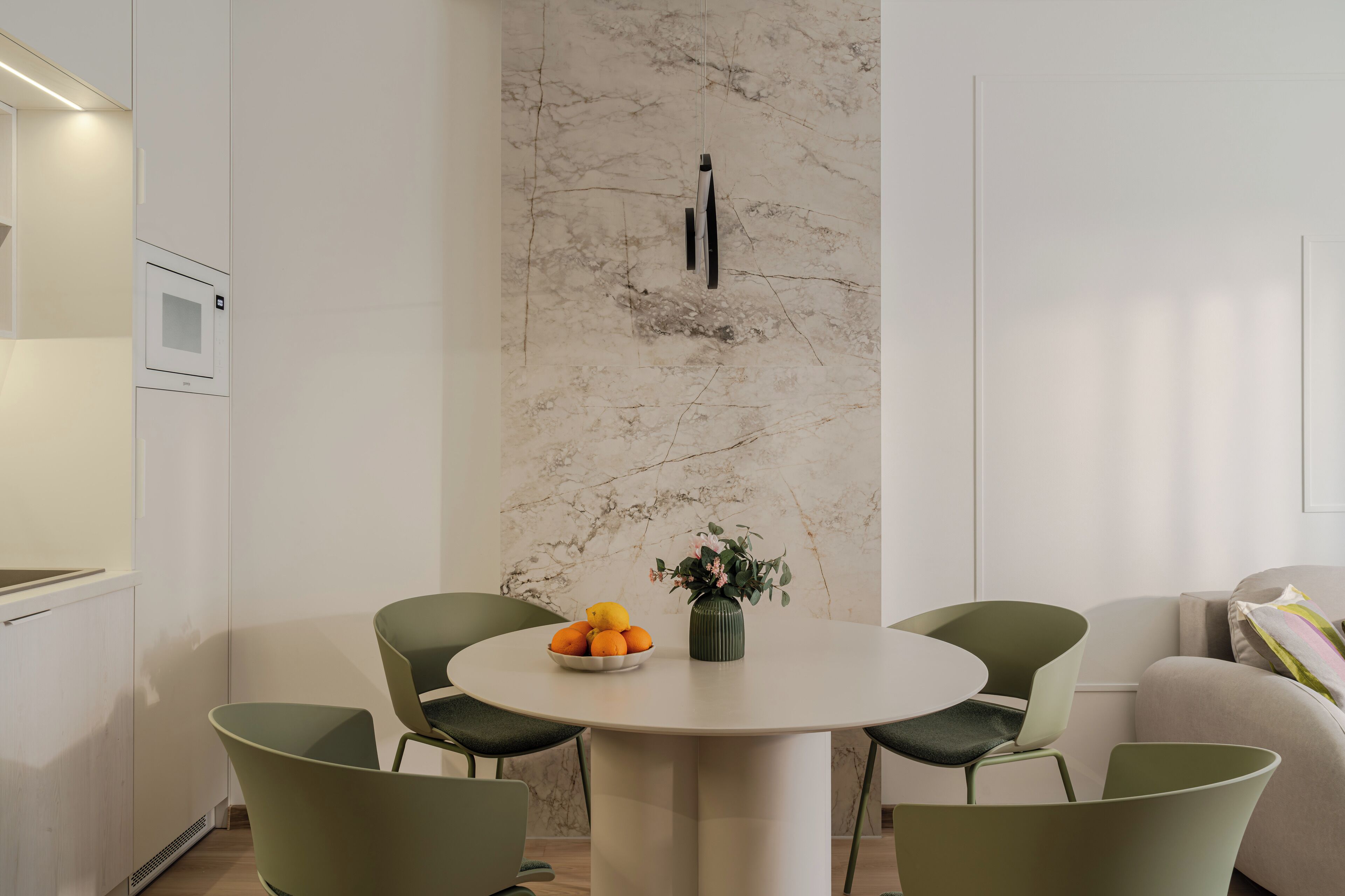 Een moderne keuken met een witte marmeren spatwand, een ronde eettafel met vier stoelen en een schaal met sinaasappels op de tafel.