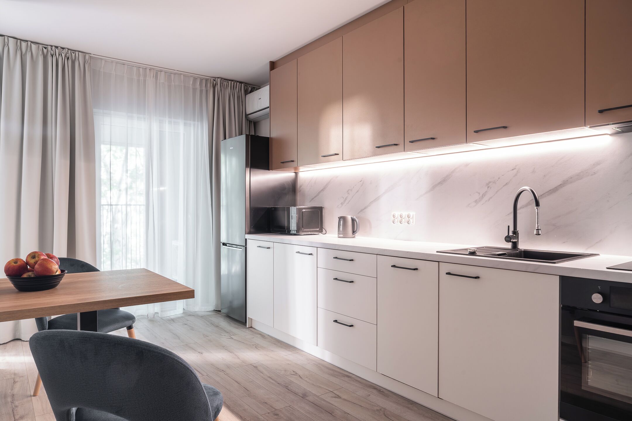 Una cocina moderna con armarios blancos, encimera de mármol y horno empotrado.