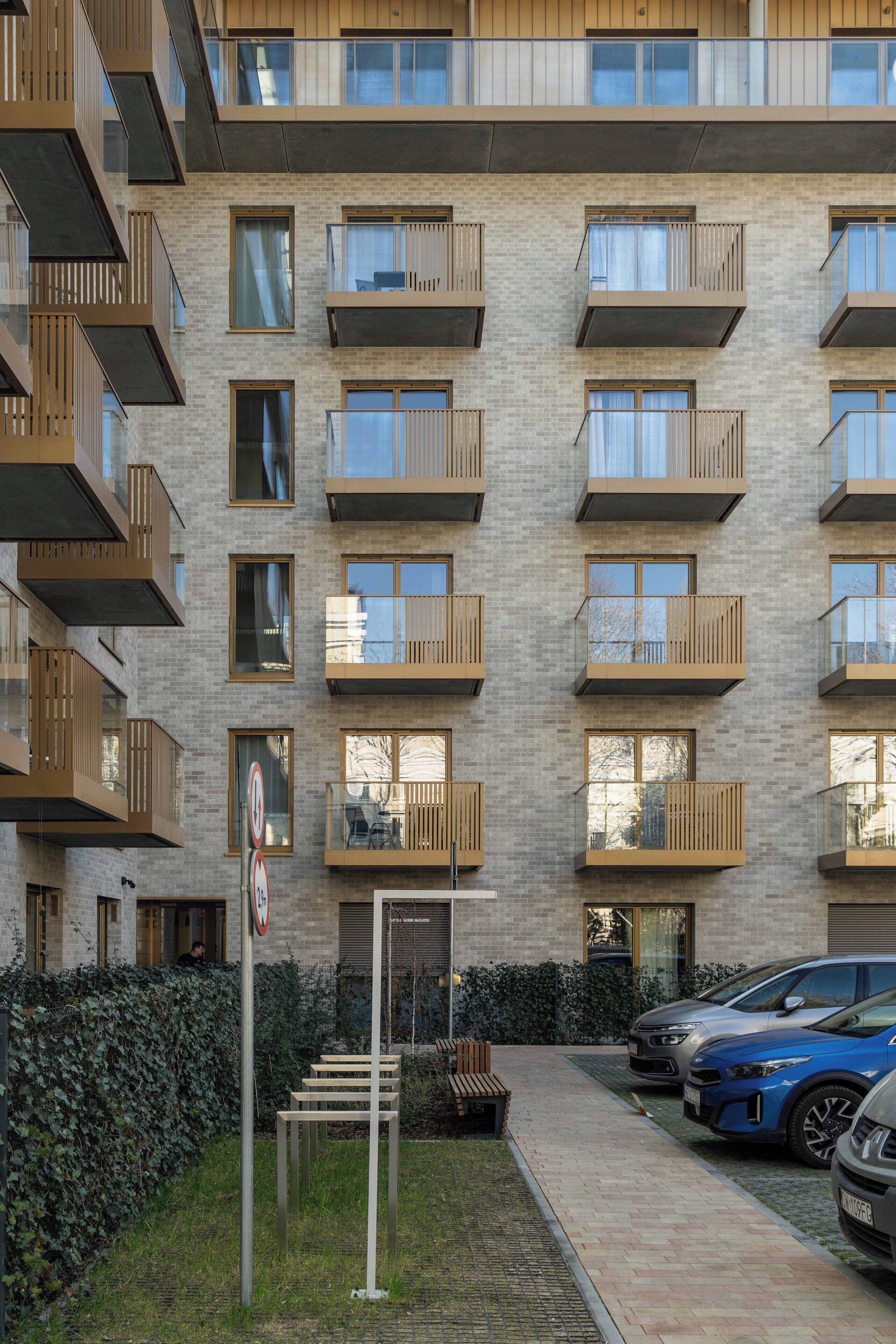 A multi-story residential building with balconies, a parking area, and a no-parking sign.