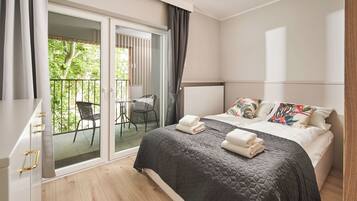 A modern bedroom with a large bed, a balcony with a chair, and a view of greenery.