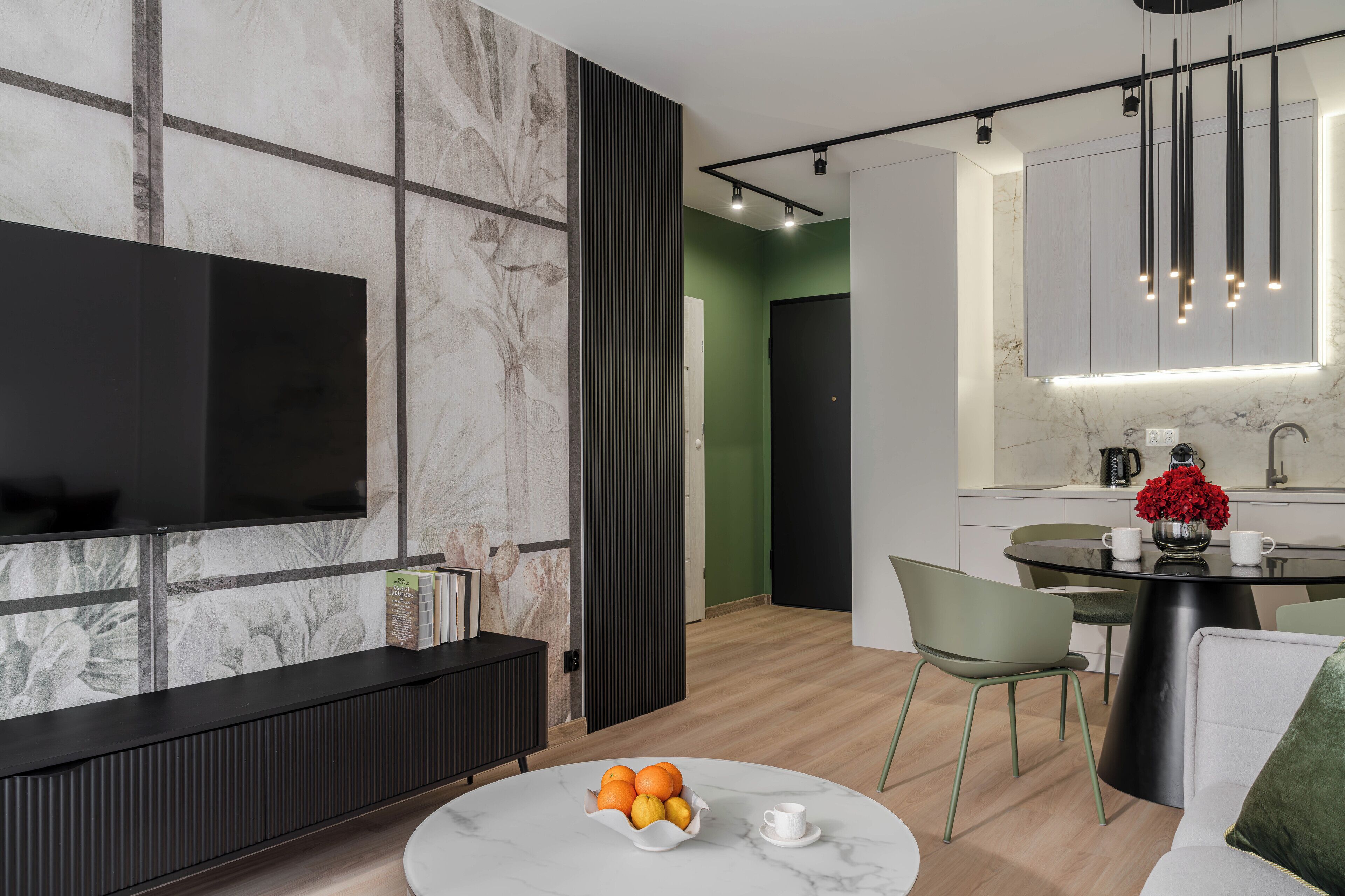 Een moderne woonkamer met een flatscreen televisie, een marmeren salontafel met fruit, en een groene bank.