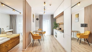 A modern hotel room with a bed, a dining area with a table and chairs, a kitchen area, and a large mirror. - Symphony Atal City Square (Wroclaw)