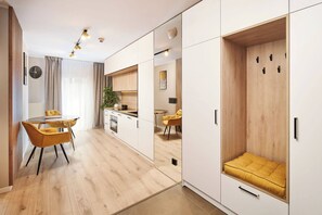 A modern kitchen with white cabinets and a wooden countertop. There is a dining area with a yellow chair and a table. - Symphony Atal City Square (Wroclaw)