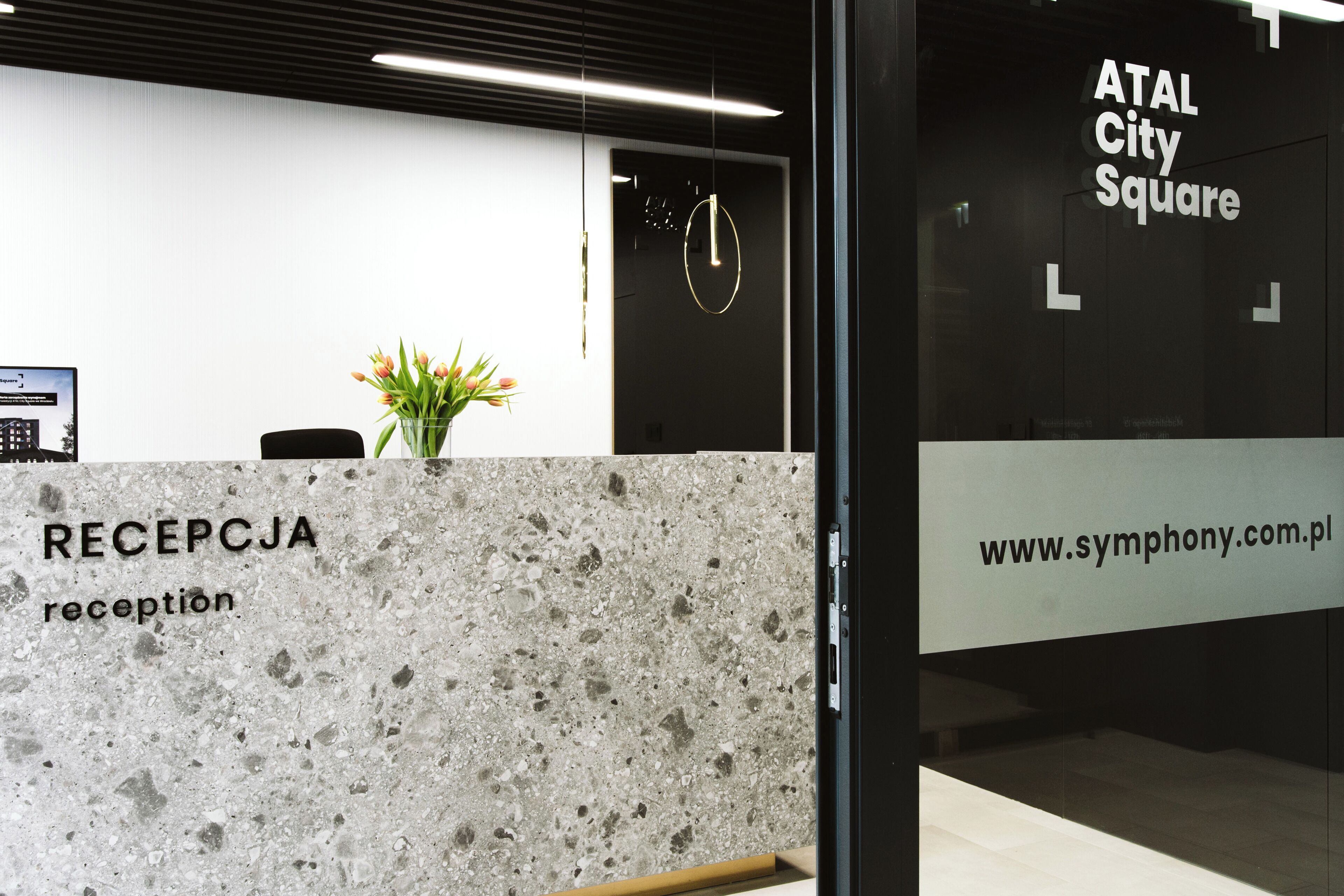 Un comptoir d’accueil avec un plateau en marbre portant l’inscription « RÉCEPTION » et une enseigne indiquant « ATAL City Square », ainsi que l’adresse du site web.