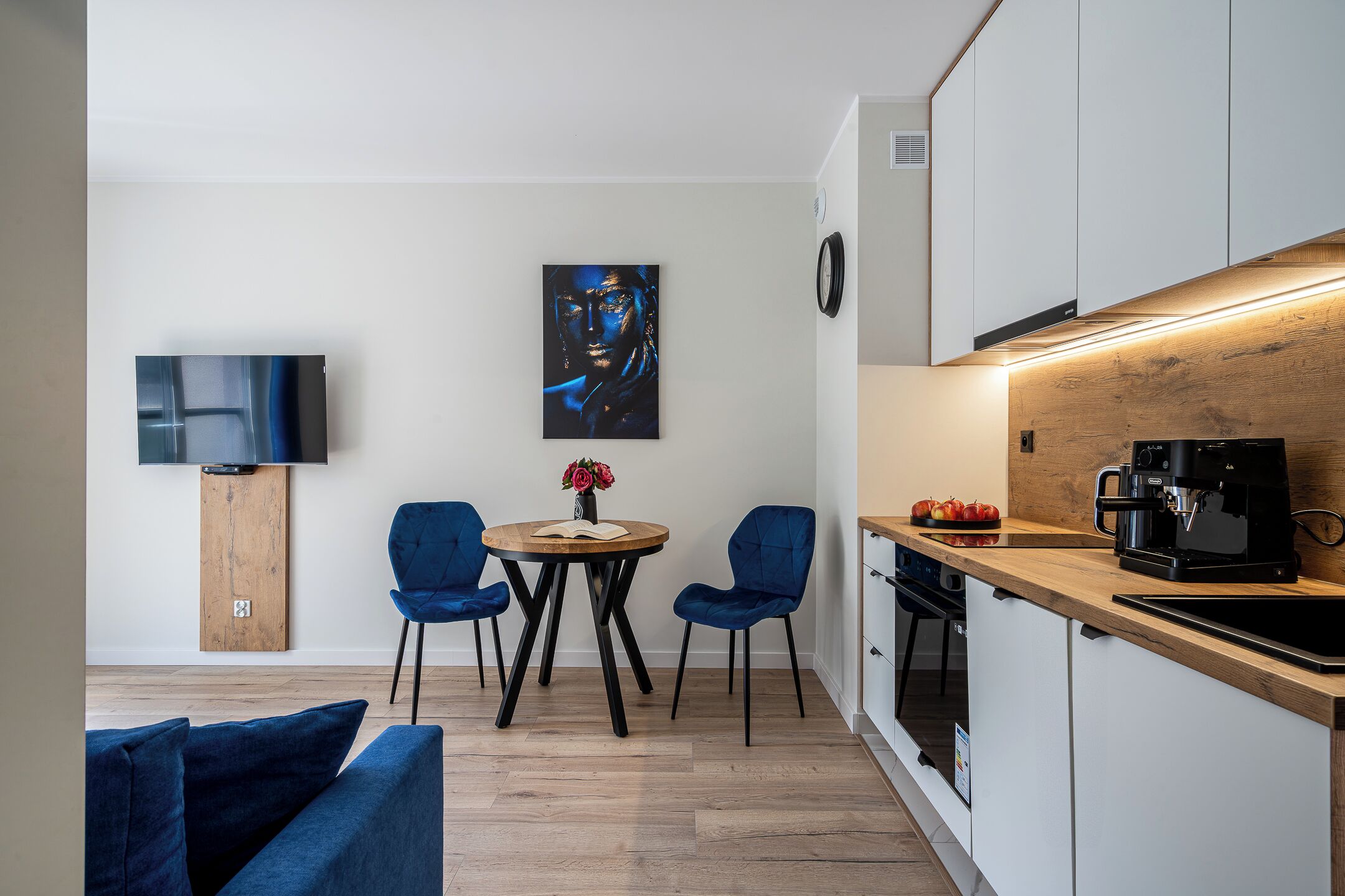 A modern kitchen with a wooden countertop, a coffee machine, and a dining area with two chairs and a table.