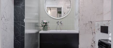 A modern bathroom with a black marble vanity, a round mirror, a toilet, and a washing machine.