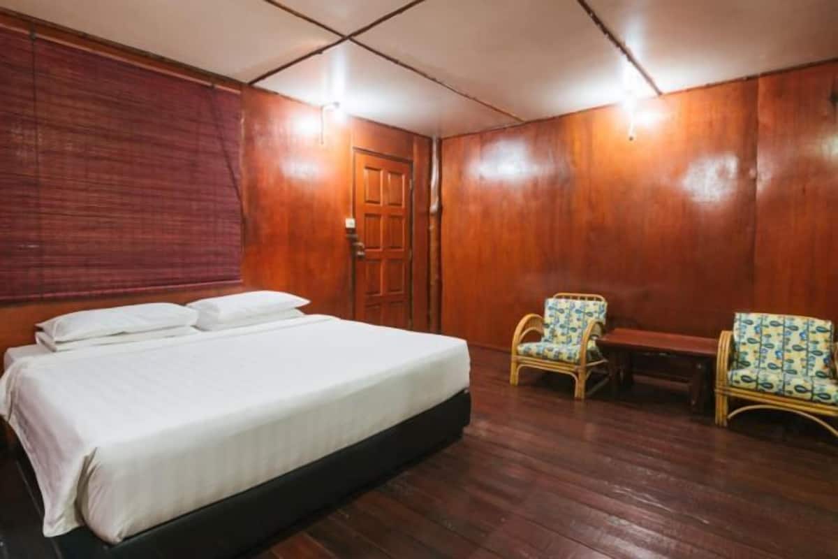 A room with a bed, two chairs, a wooden door, and a window with blinds.