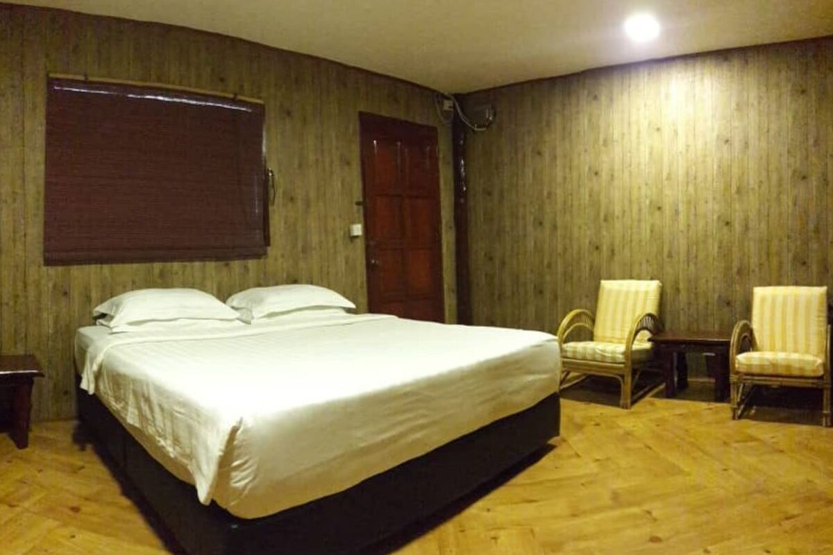 A room with a large bed, two chairs, a small table, and a wooden floor.