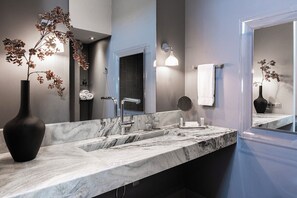 Un baño moderno con lavamanos de mármol, un espejo grande y plantas decorativas.