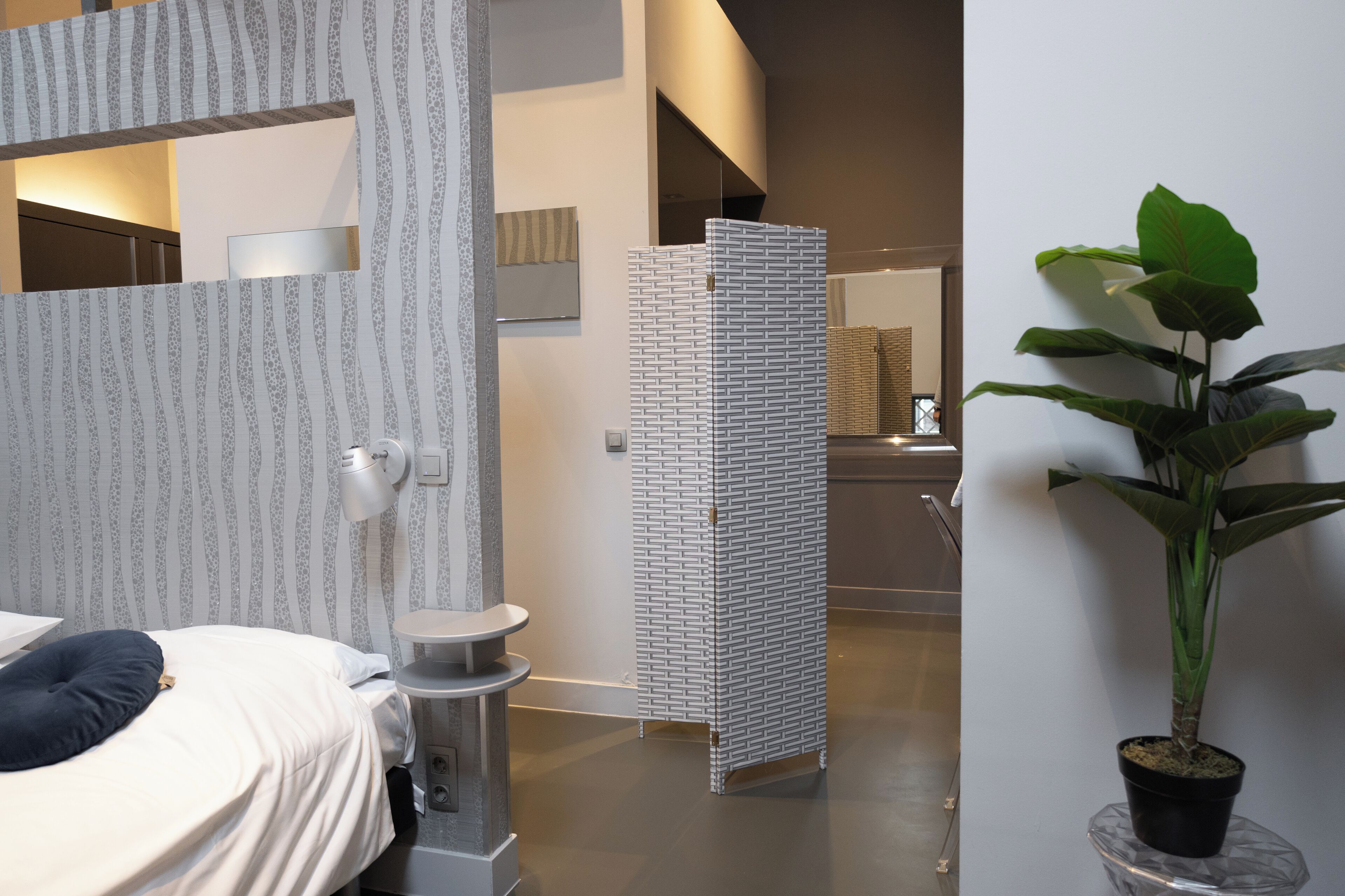 A modern hotel room with a bed, a small round table, a potted plant, and a patterned partition.