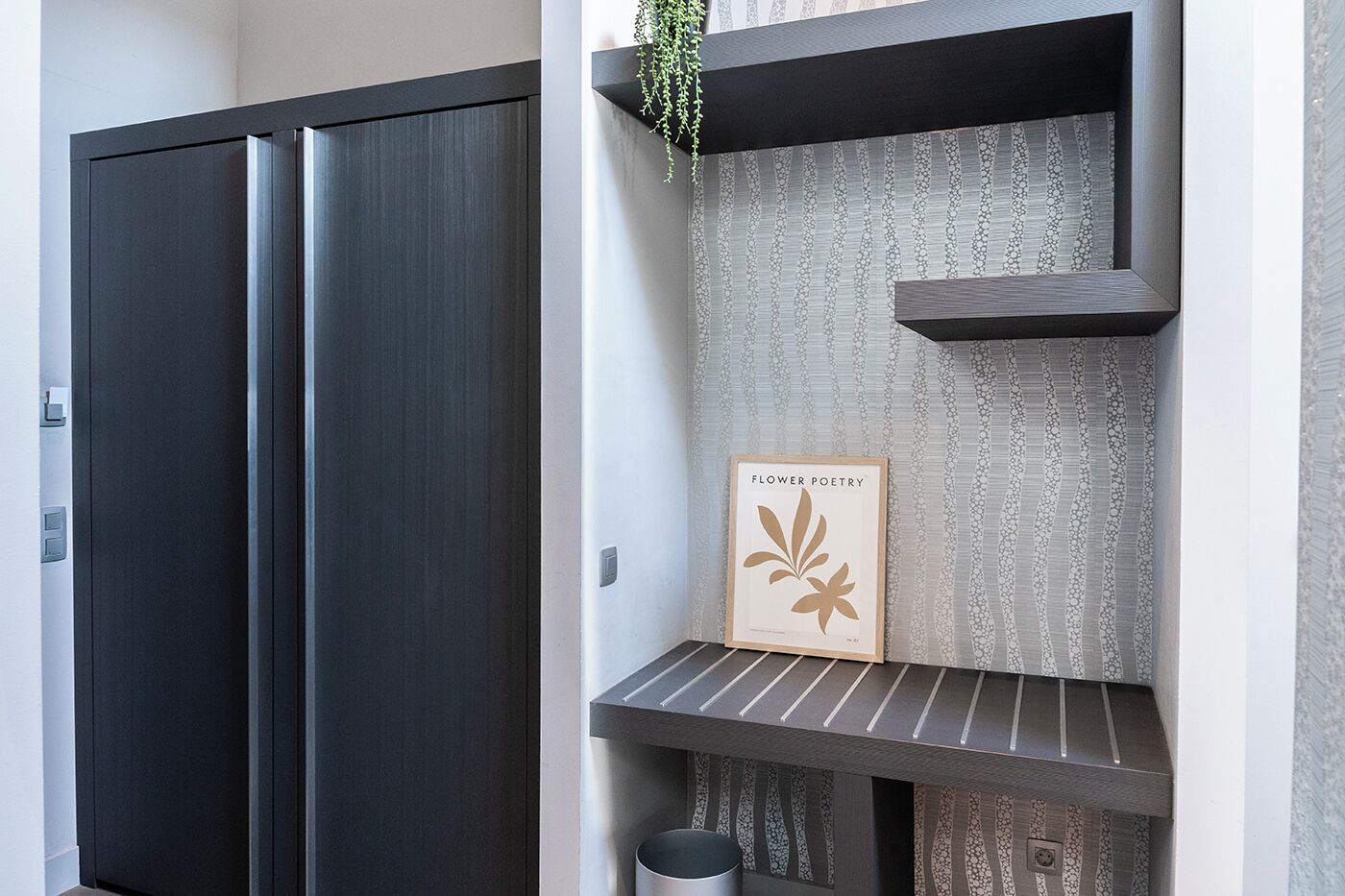 Un intérieur moderne avec une porte en bois foncé, un mur à texture et une étagère sur laquelle est posée une image encadrée intitulée « Poésie florale ».