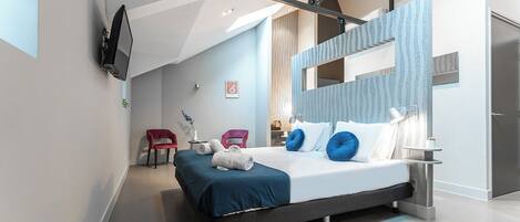 A modern bedroom with a large bed, two red chairs, a TV mounted on the wall, and a mirror with a patterned frame.