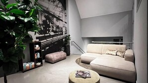 Un salon moderne avec un canapé, un pouf et une bibliothèque.