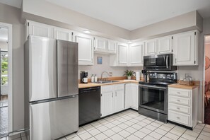 A modern kitchen with stainless steel appliances, white cabinetry, and a tiled floor. - Spacious Family & Work-Friendly 3BD w/ Workspace, Fire Pit & Park Views Near Campus (Champaign)
