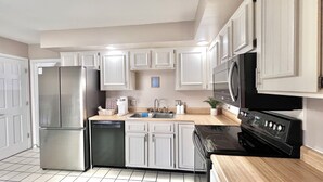 A modern kitchen with white cabinets, stainless steel appliances, and a wooden countertop.