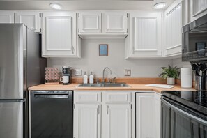 A modern kitchen with white cabinetry, a stainless steel refrigerator, a Bosch dishwasher, a coffee maker, and a sink with a wooden countertop.