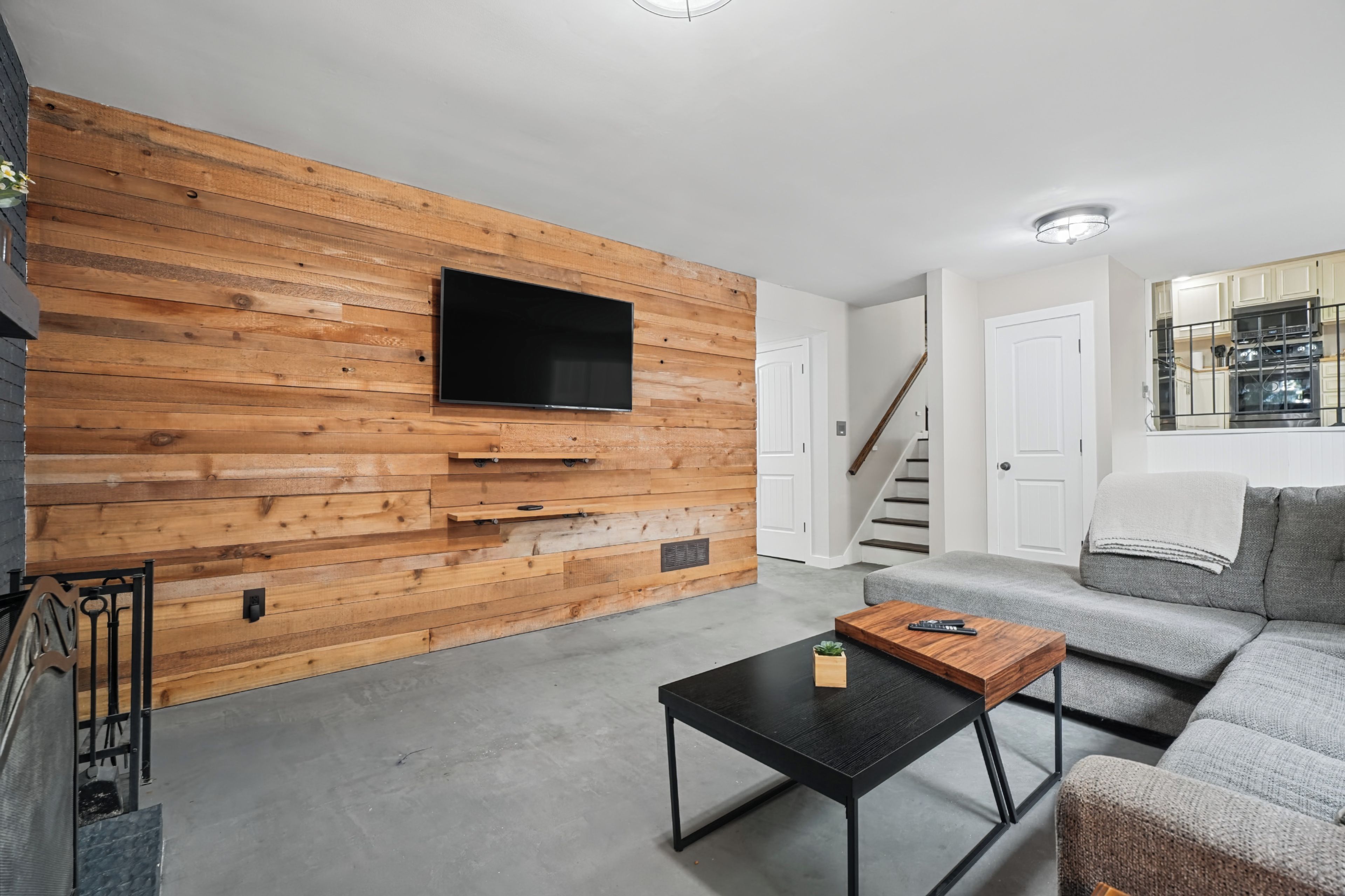 A modern living room with a wooden accent wall, a flat-screen TV, a black coffee table, and a grey sofa.
