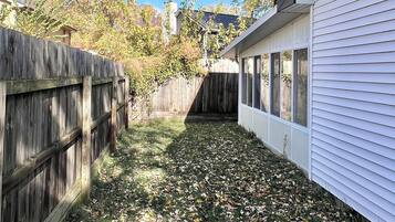 Un patio trasero con valla de madera, un edificio blanco y árboles con hojas otoñales.