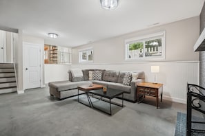 A living room with a sectional sofa, a coffee table, a side table with a lamp, and a staircase leading to an upper level.
